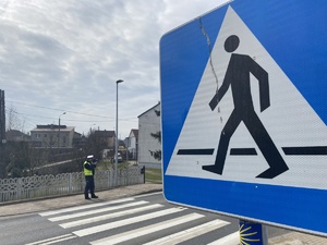 na zdjęciu widoczny znak informacyjny przejście dla pieszych, w oddali policjant przy przejściu w trakcie pomiaru prędkości