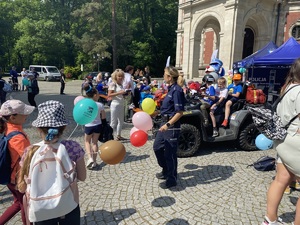 na zdjęciu policjantka z balonami w rękach, przy quadzie, na którym siedzą dzieci