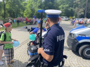 na zdjęciu policjant przy motorze, w tle dzieci
