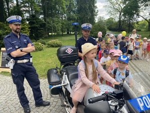 na zdjęciu policjanci przy motocyklu, na którym siedzi dziecko, w tle inne dzieci czekające w kolejce