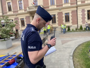 na zdjęciu policjant trzymający w ręku radiostację, w tle urząd