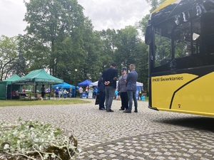 na zdjęciu róg elektrycznego autobusu przy którym stoją osoby i komendant