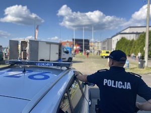 na zdjęciu policjant przy radiowozie, obserwuje teren imprezy