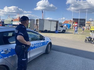 na zdjęciu policjant przy radiowozie, obserwuje teren imprezy