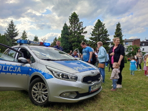 na zdjęciu radiowóz, obok dzieci z rodzicami i policjant