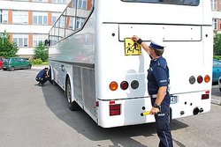 na zdjęciu policjant przy autobusie trzyma w ręku znak uwaga dzieci
