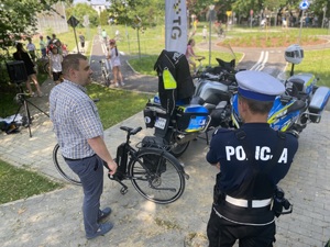 na zdjęciu policjanci i inny mężczyzna przy motocyklu, w tle dzieci na drogach miasteczka ruchu drogowego