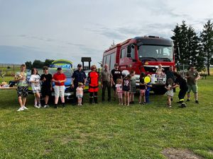 na zdjęciu uczestnicy spotkania z policjantem, strażakami, leśnikami i pielęgniarką, którzy stoją przed radiowozem i wozem strażackim