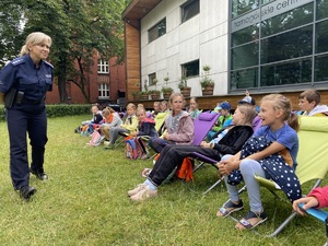 na zdjęciu dzieci na leżakach przed budynkiem, a przed nimi policjantka