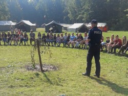 na zdjęciu policjant przed grupą dzieci, które siedzą na trawie