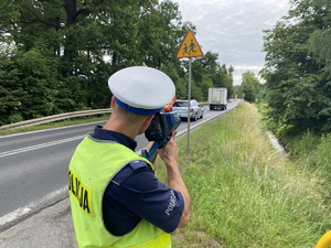 na zdjęciu policjant przy drodze z miernikiem prędkości, w tle auta