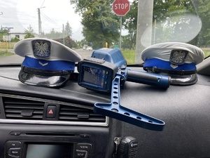 na zdjęciu podszybie samochodu, na której są dwie czapki policyjne i miernik prędkości