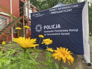 na zdjęciu kwiatki i bok policyjnego namiotu koloru niebieskiego, na którym widać napis Komenda Powiatowa Policji w Tarnowskich Górach