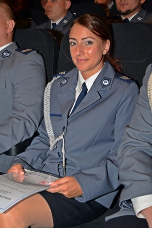 na zdjęciu policjantka w mundurze siedząca na widowni, w ręku trzyma akt mianowania