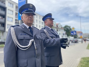 na zdjęciu komendant powiatowy i jego zastępca przed tablicą pamiątkową, komendant trzyma w ręku znicz