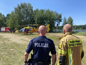 na zdjęciu policjant i strażak, przed nimi śmigłowiec ratunkowy