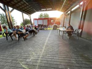 na zdjęciu dzielnicowy na przeciw mieszkańców w trakcie spotkania, z tyłu wóz strażacki