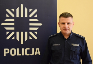 dzielnicowy Kopeć przy banerze z napisem policja