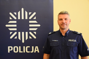 dzielnicowy Syrnik przy banerze z napisem policja