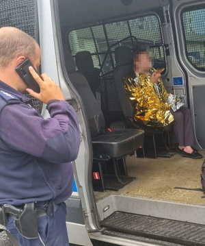 na zdjęciu policjant rozmawia przez telefon przy radiowozie, w którym siedzi zaginiona okryta kocem termincznym