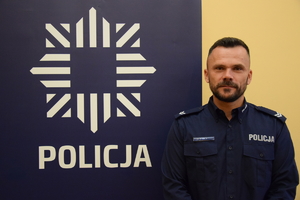 dzielnicowy Kracik przy banerze z napisem policja