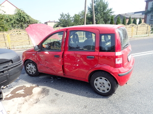 na zdjęciu czerwonych samochód na środku jezdni z uszkodzonym lewym bokiem