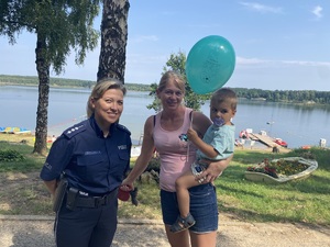 na zdjęciu policjantka stoi obok matki z dzieckiem, które w ręce trzyma balon