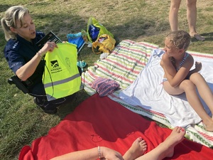 na zdjęciu dziecko na kocu, a obok policjantka wręczająca odblaskową torbę
