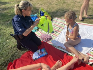 na zdjęciu dziecko na kocu, a obok policjantka wręczająca odblaskową torbę