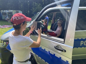 na zdjęciu rodzic robiący telefonem zdjęcia swojemu dziecku, które siedzi w radiowozie