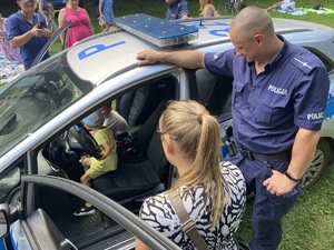 na zdjęciu policjant i rodzic przy radiowozie obserwują dziecko które siedzi w środku