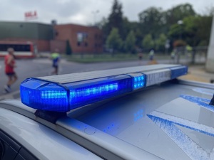 na zdjęciu policyjny neon świecący się na niebiesko, a za nim widocznie osoby, które biegną po jezdni