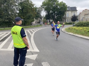 na zdjęciu policjant na jezdni, obok niego przebiegają uczestnicy zawodów