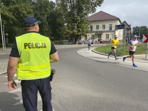 na zdjęciu policjant na jezdni, obok niego przebiegają uczestnicy zawodów
