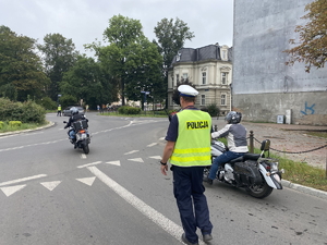 na zdjęciu policjant na jezdni, a obok niego dwa motocykle wjeżdżające na rondo