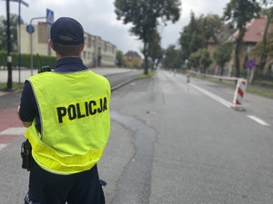 na zdjęciu policjant w kamizelce odblaskowej na jezdni, zwrócony w kierunku trasy biegu