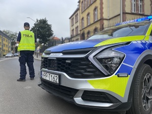 na zdjęciu przód policyjnego radiowozu, przy którym tyłem stoi policjant