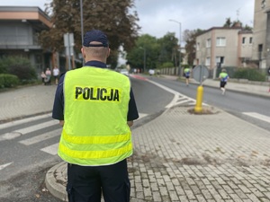 na zdjęciu policjant stojący przy drogowej wyspie, za którą widoczni są biegacze