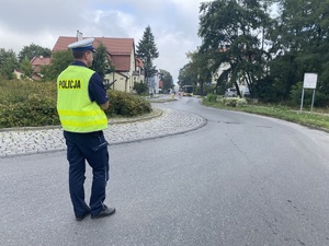na zdjęciu policjant na rondzie z radiostacją w ręku, w tle jadący w jego kierunku autobus miejski