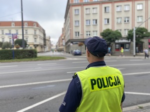 na zdjęciu policjant w kamizelce odblaskowej obserwuje trasę biegu prowadzącą na tarnogróski rynek