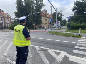 na zdjęciu policjant z radiostacją w ręku na skrzyżowaniu, po którym biegną uczestnicy zawodów