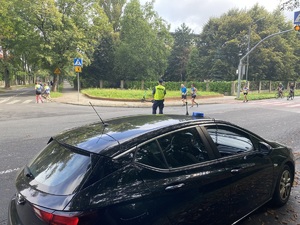 na zdjęciu policyjny nieoznakowany radiowóz z neonem na dachu, przed nim policjant obserwujący biegaczy na trasie zawodów