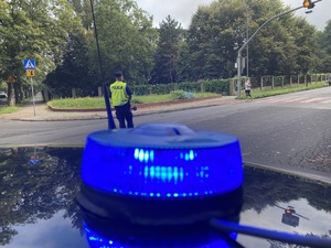 na zdjęciu policyjny neon emitujący niebieskie światło, za którym widać stojącego na jezdni policjanta