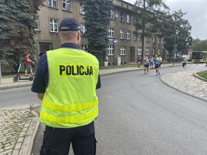 na zdjęciu policjant stojący na rondzie, obserwuje biegaczy