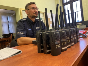 na zdjęciu naczelnik wydziału ruchu drogowego siedzący przy biurku, na którym ułożone są radiostacje