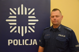 dzielnicowy Szypuła przy banerze z napisem policja