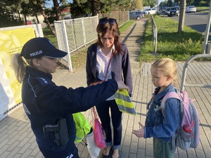 na zdjęciu policjantka przekazuje dzieciom odblaskowe gadżety
