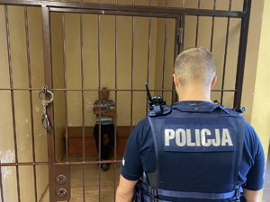 na zdjęciu policjant stoi przy celi, w której siedzi zatrzymany mężczyzna