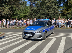 na zdjęciu policyjny radiowóz z włączonymi niebieskimi sygnałami błyskowymi na jezdni, za nim widownia