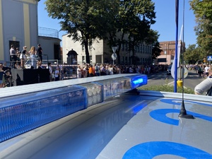 na zdjęciu policyjny neon emitujący niebieskie światło, w tle widownia, która obserwuje pochód
